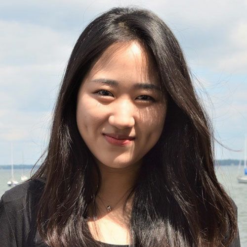 A woman with long black hair is standing in front of a body of water.