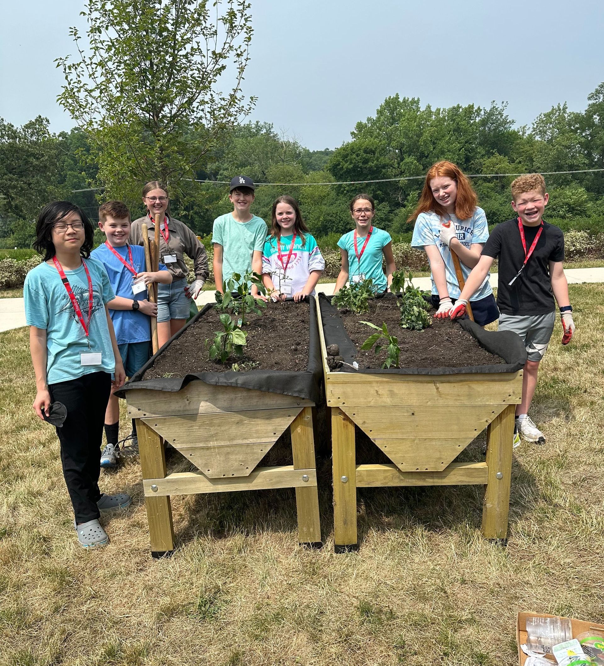 A group of young people are standing next to wooden planters in a field.