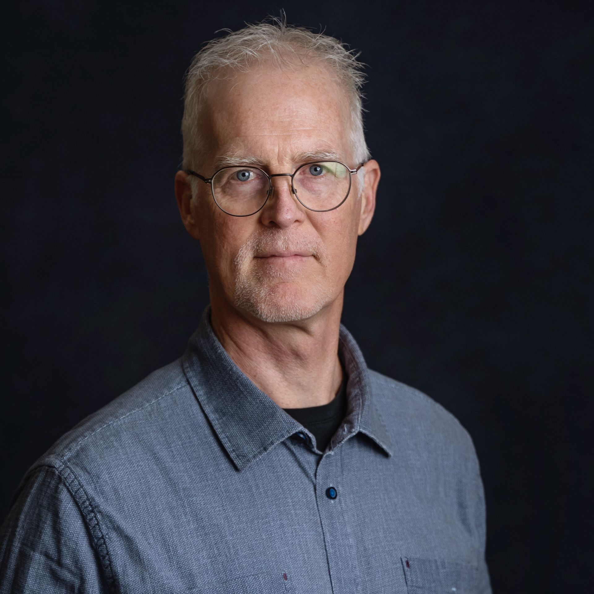 A man wearing a floral shirt and sunglasses is smiling in front of a city skyline.