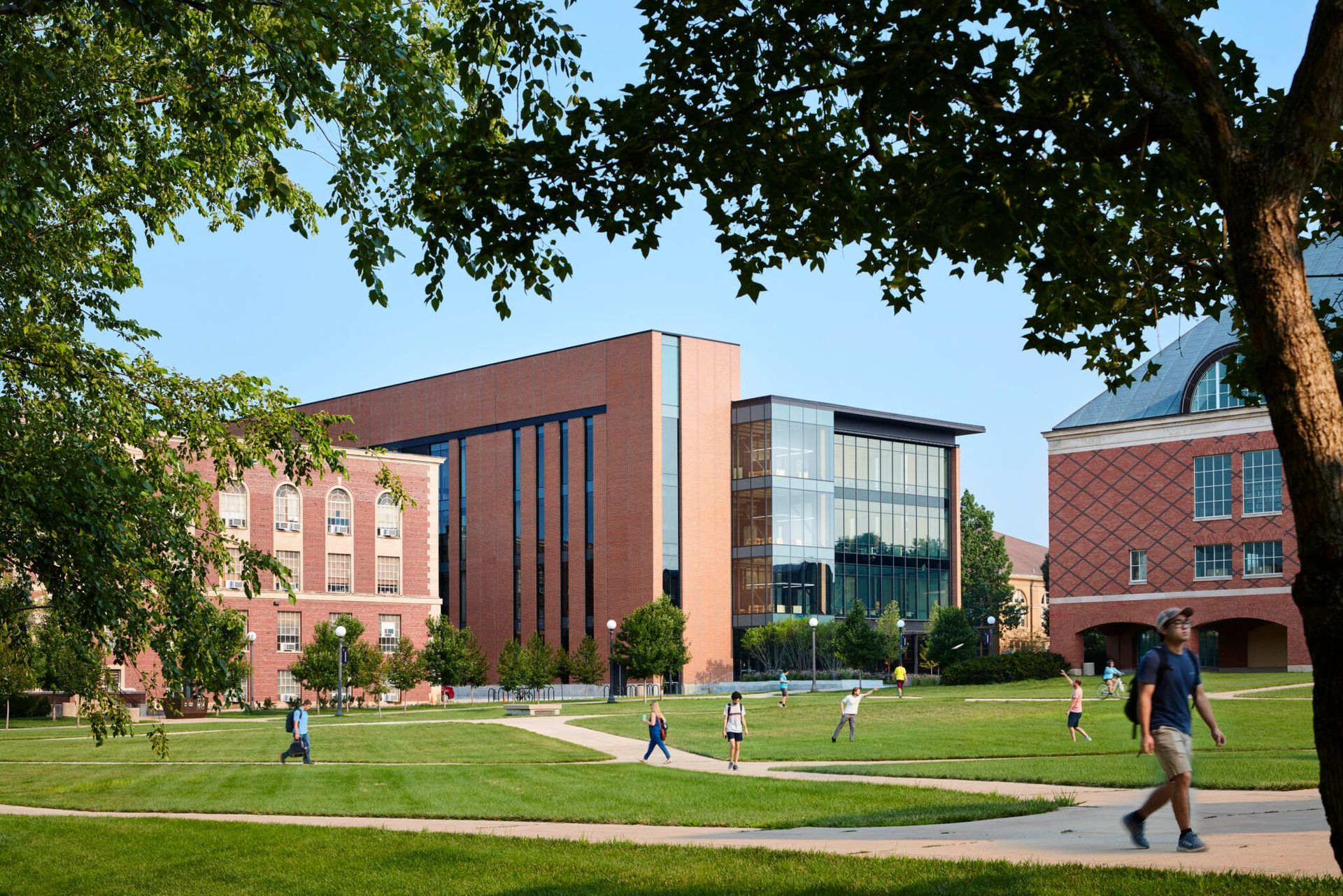 A group of people are walking through a grassy field in front of a large brick building