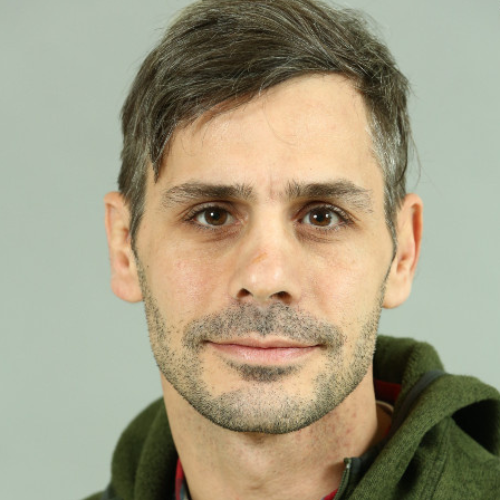 A man with a beard and a green hoodie is smiling for the camera.