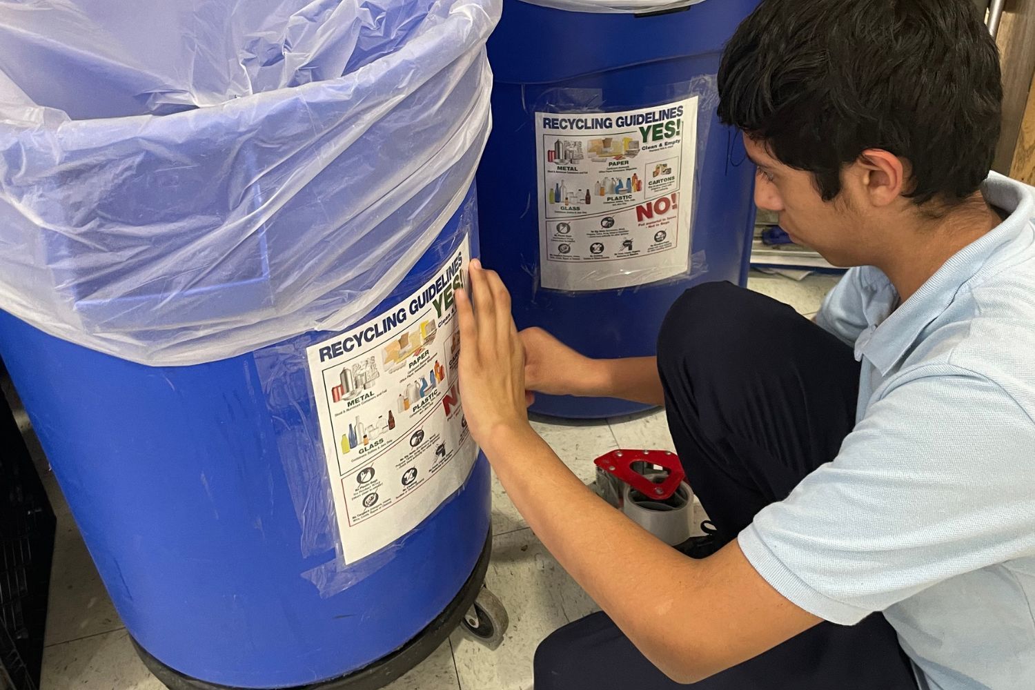 A man is kneeling down next to a blue trash can.