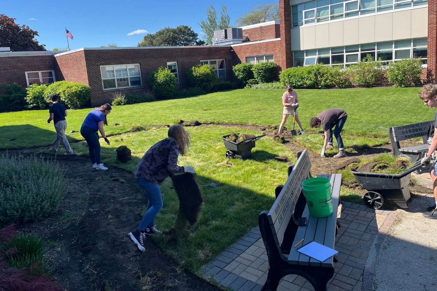 A group of people are working in a garden in front of a building.