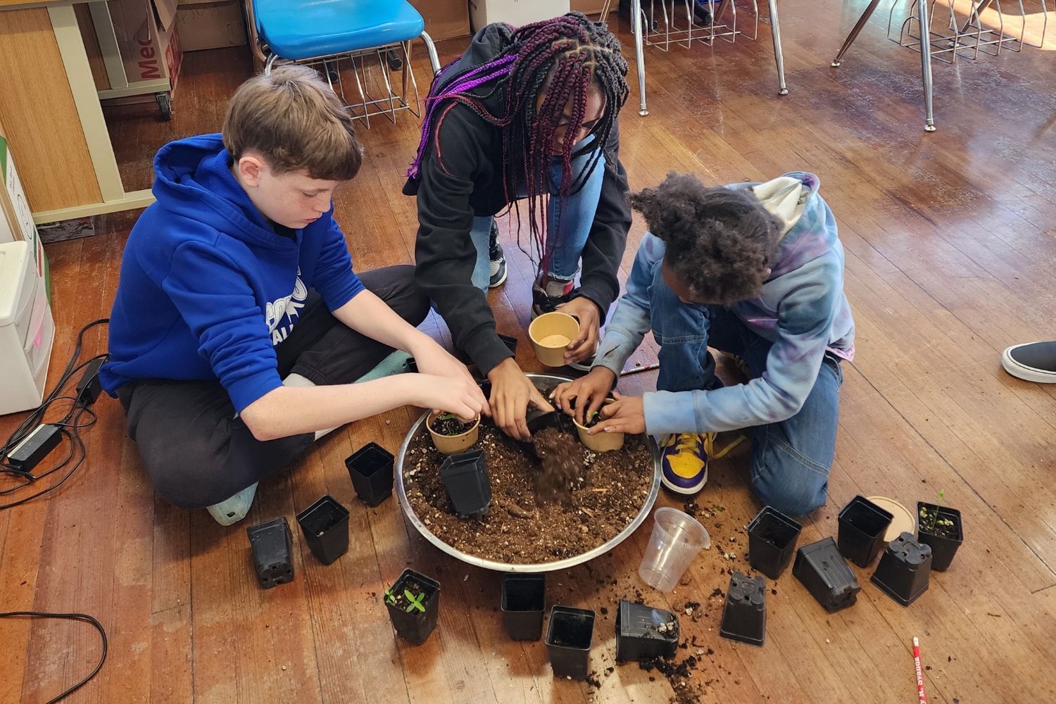 A group of children are sitting on the floor planting potted plants.