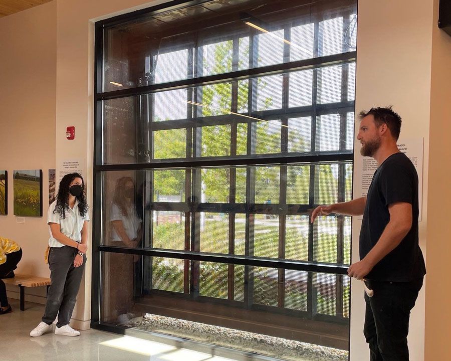 A man and a woman are standing in front of a large window.