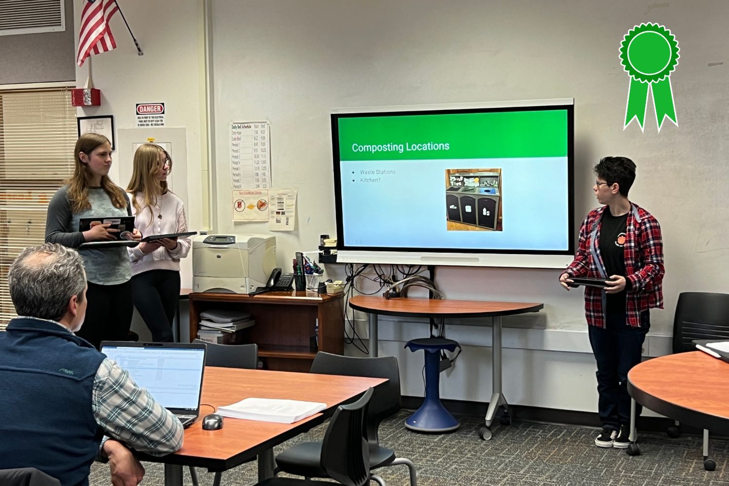 A group of people are sitting at tables in front of a large screen.