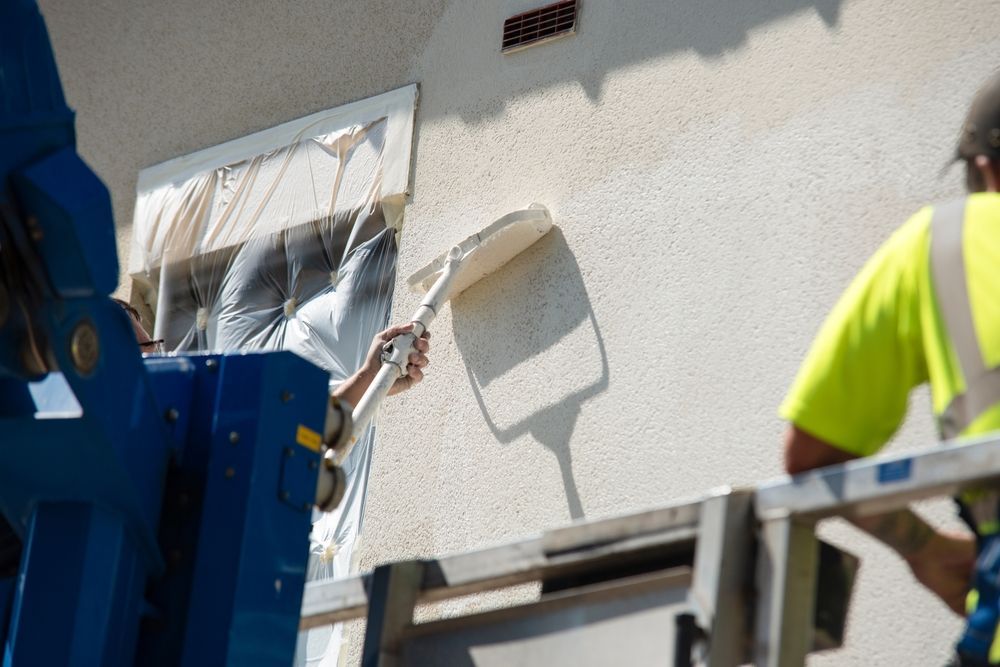 Workers applying stucco to a building's exterior from a lift.