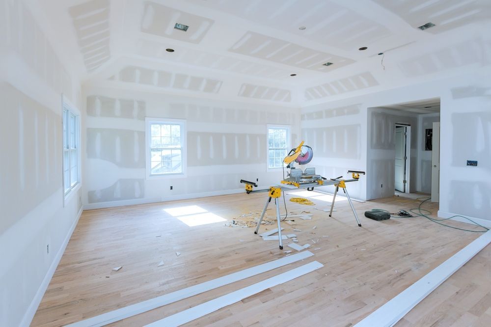 Unfinished room with drywall, windows, a saw, and trim on a wood floor.