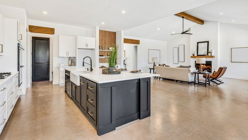 Open-concept kitchen with a black island, white cabinets, and living room with a fireplace and beige sofa.