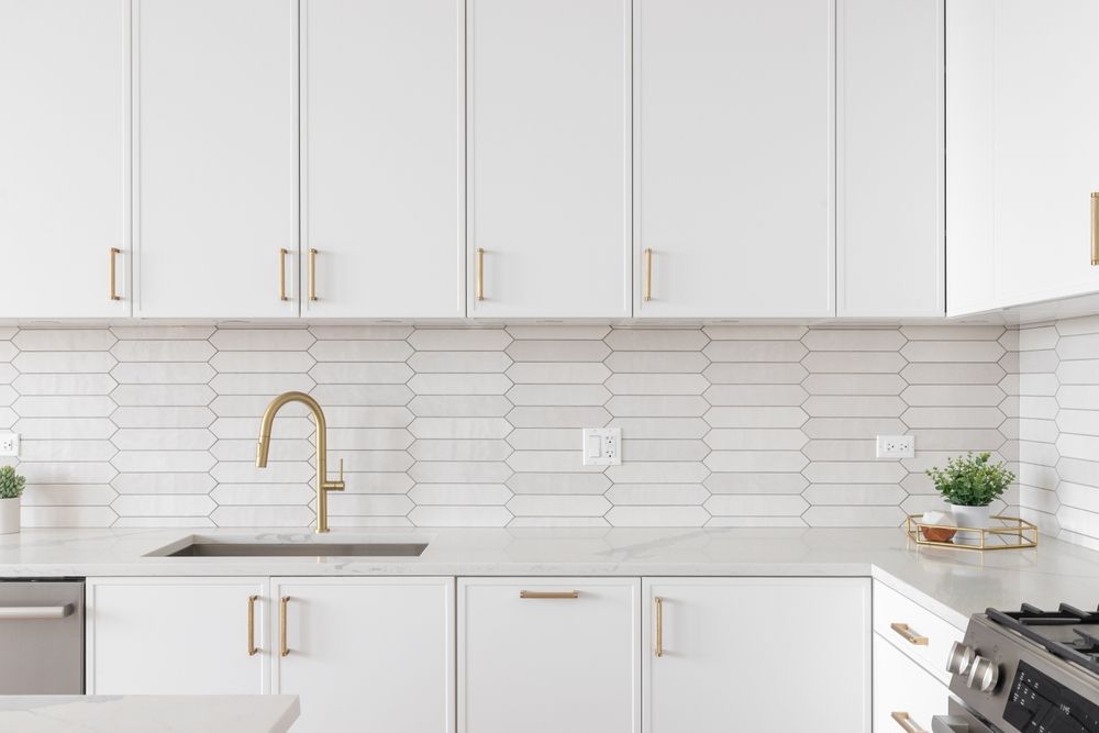 White kitchen with gold accents: cabinets, faucet, handles, and backsplash.