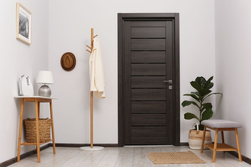 A hallway with a dark door, coat rack, small table, and potted plant against white walls.