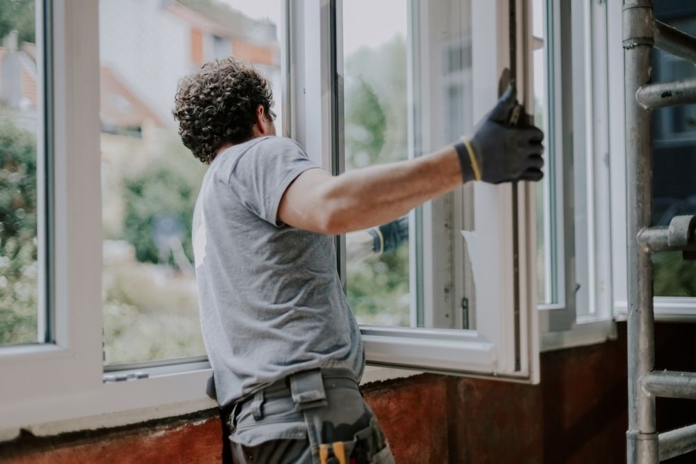 Man in gloves installing a white window in a building.