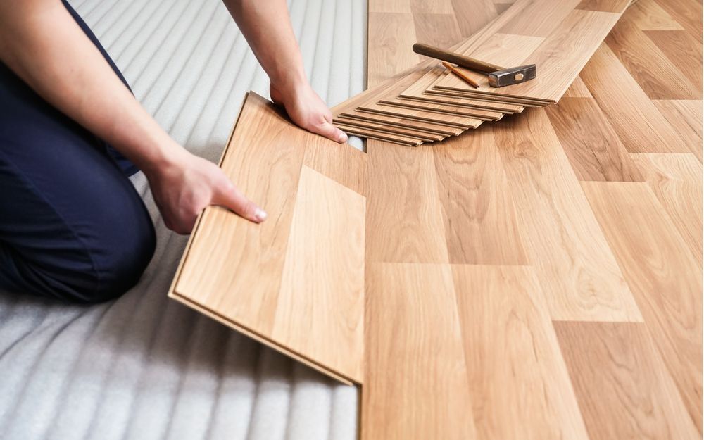 Person installing wood flooring; holding plank above a partially installed floor.