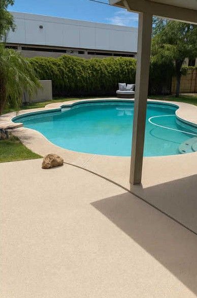 A turquoise pool with a tan patio, trees, and a white couch in the background.