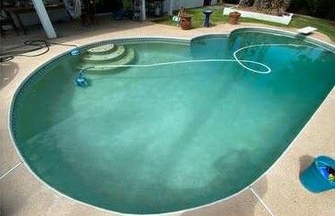 A partially filled, greenish swimming pool with steps and a pool cleaner on the bottom.