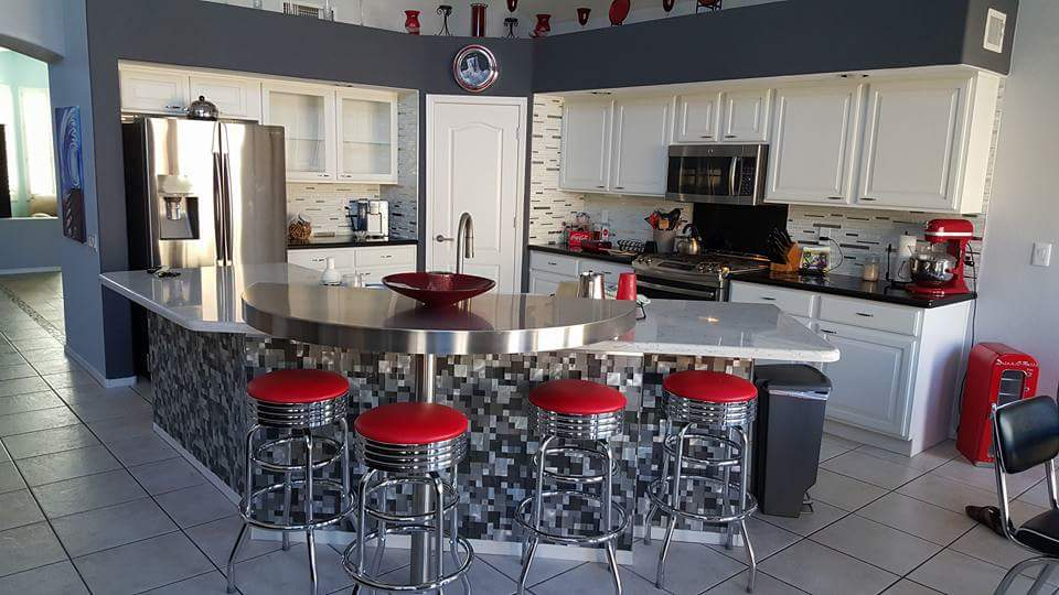 Kitchen with white cabinets, stainless steel island, and red stools.