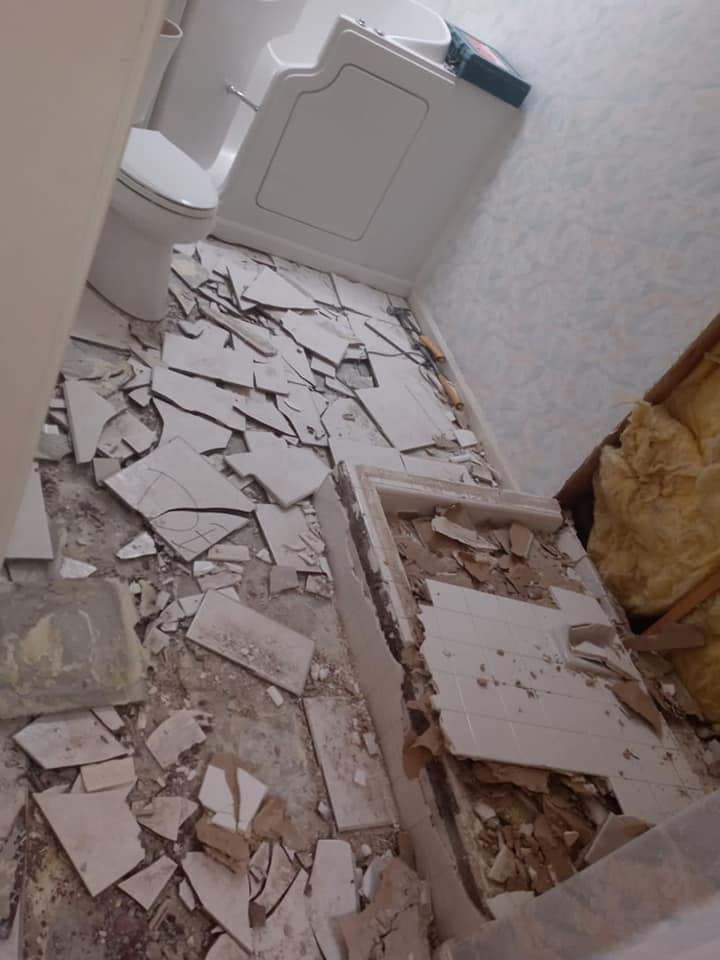 Bathroom with shattered white floor tiles; toilet visible; drywall and insulation exposed at the right.