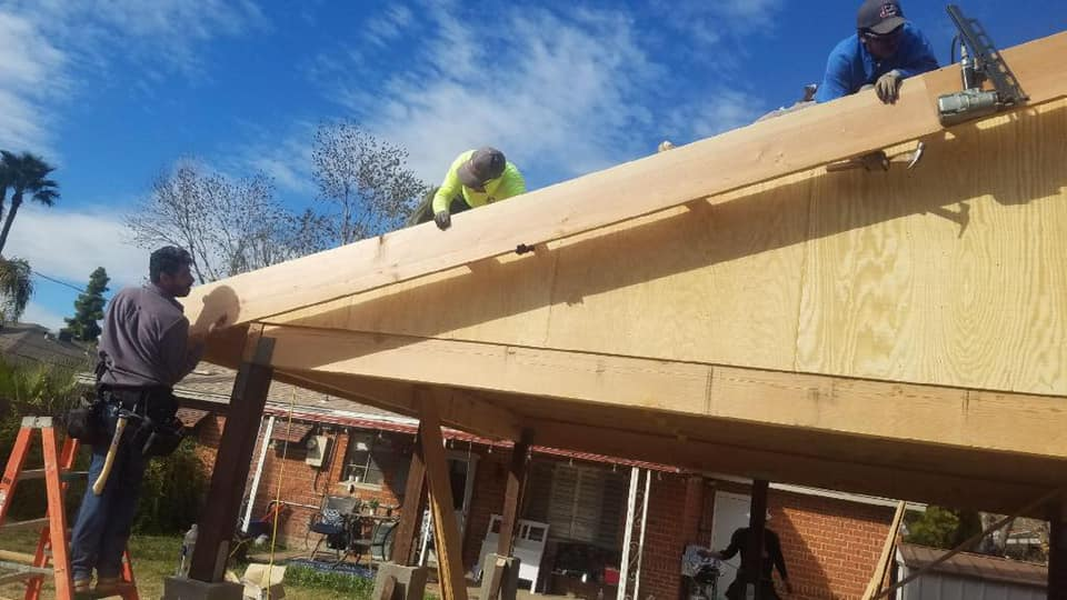 Construction workers building a wooden roof structure outdoors on a sunny day.