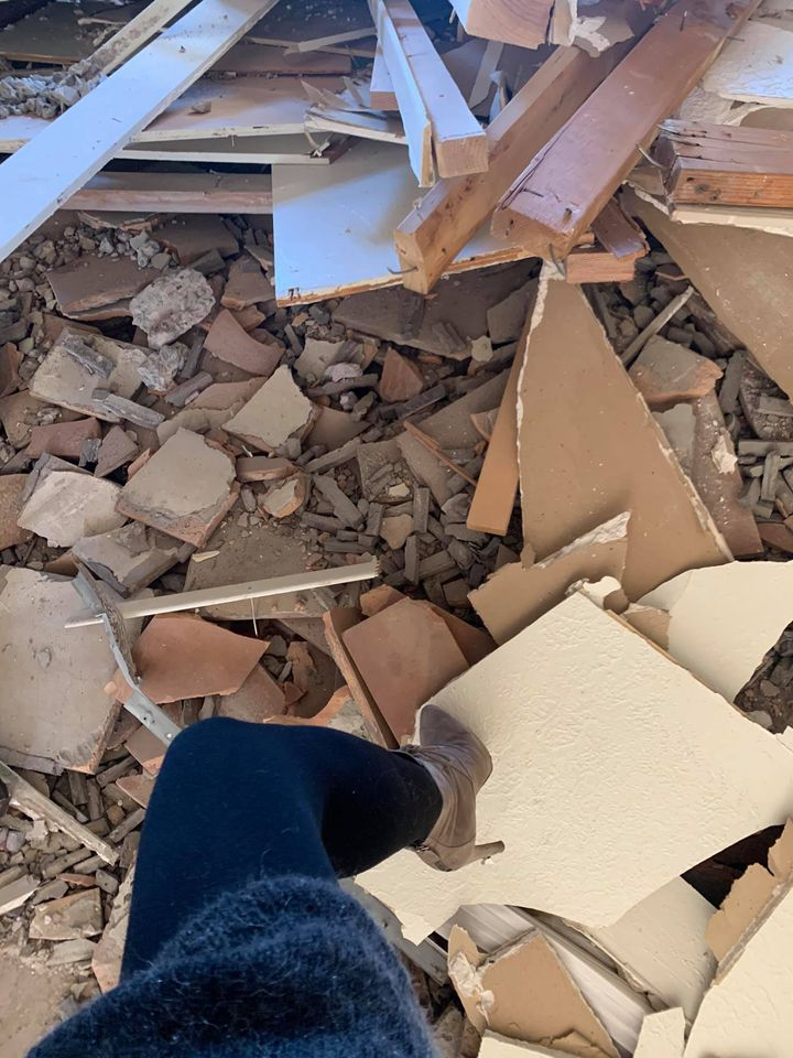 A person's leg in black pants and a gray boot stands on debris in a room; demolition site.