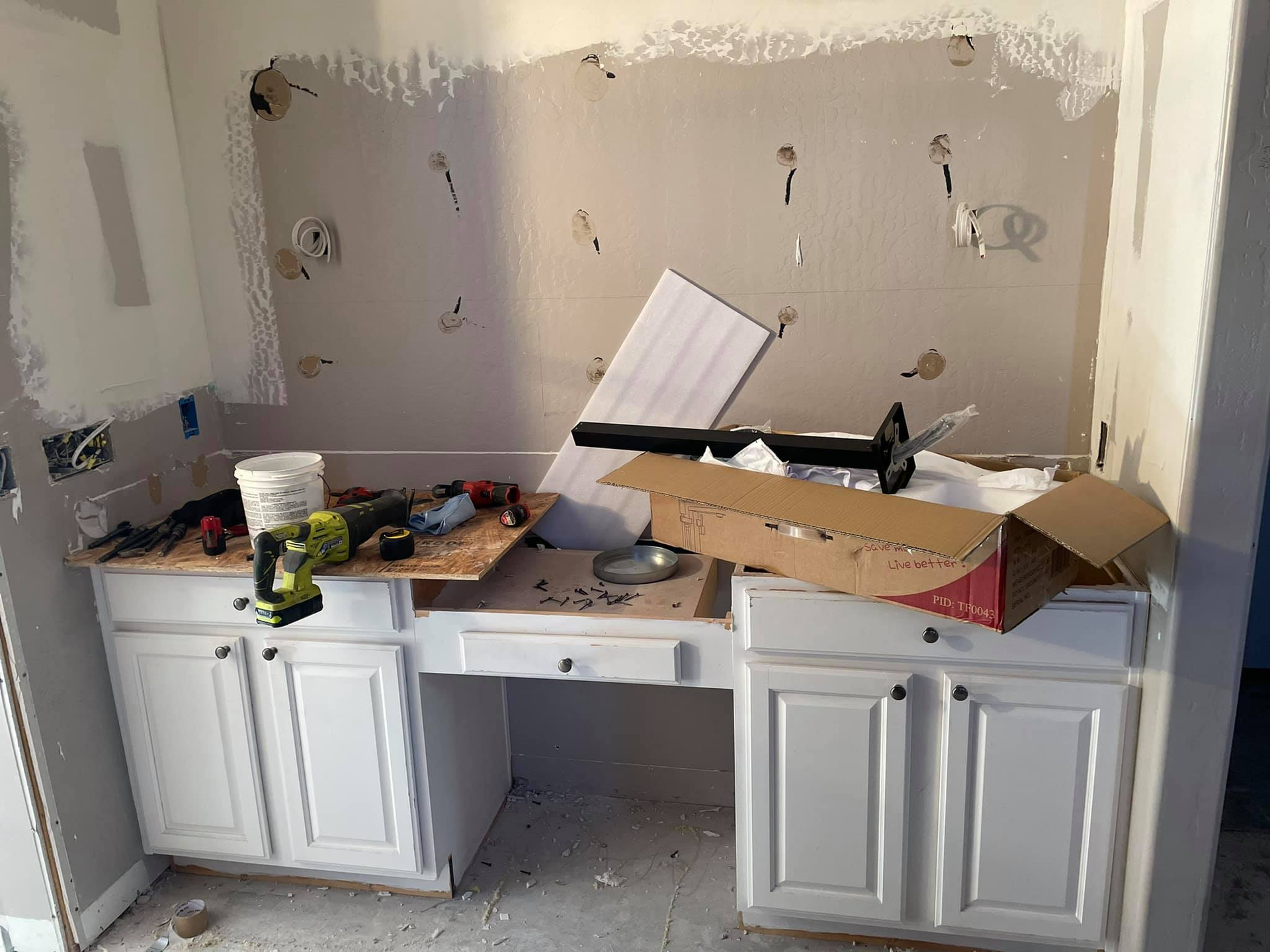 White cabinets with a desk area under construction, tools and supplies on top.