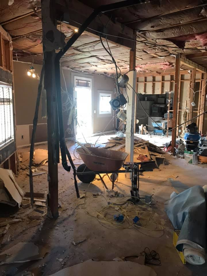 Interior of a house under renovation, with exposed studs, a wheelbarrow, and scattered debris.