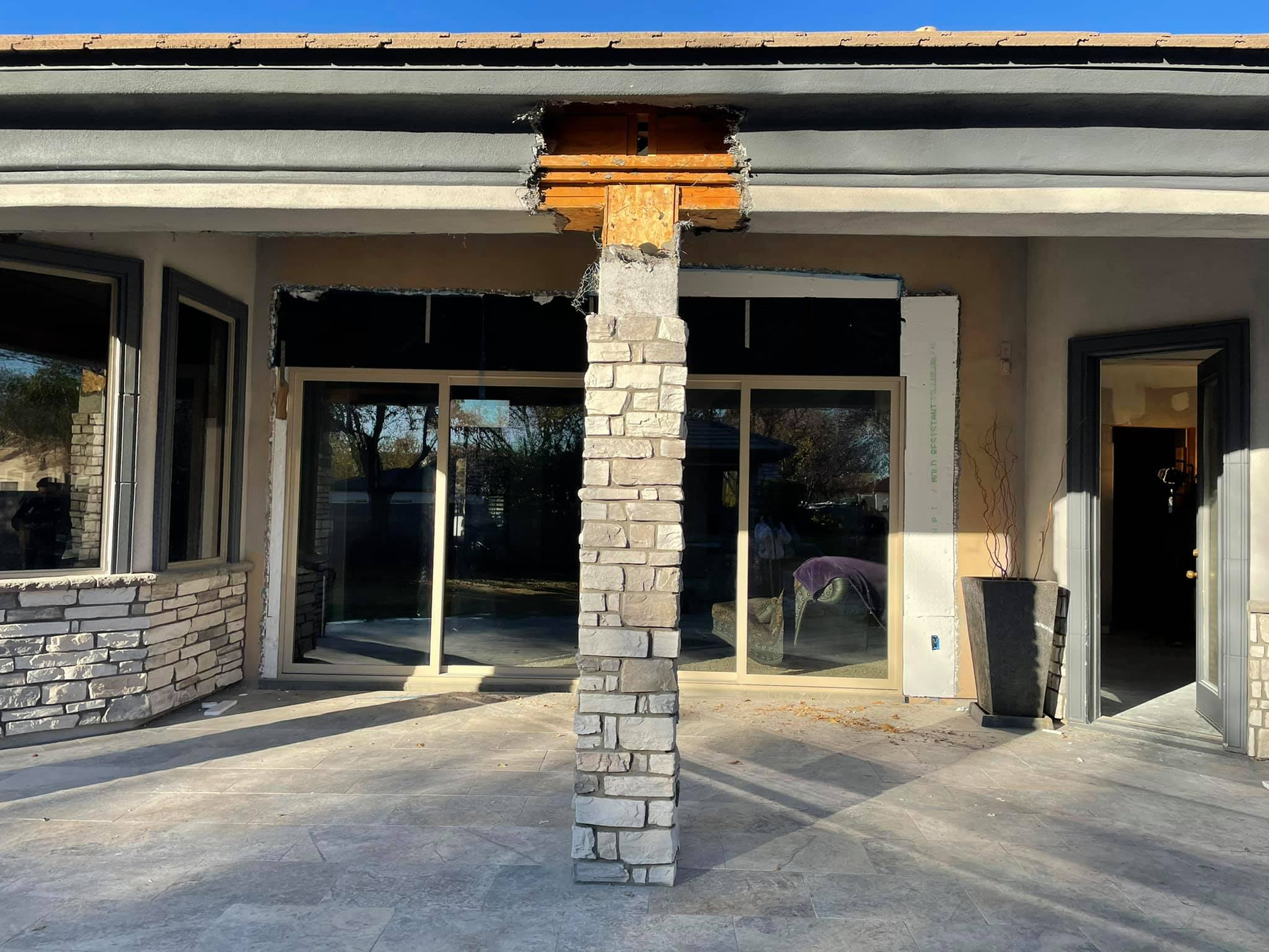 Exterior of a building under construction. Stone column supporting roof, large windows and door frames.
