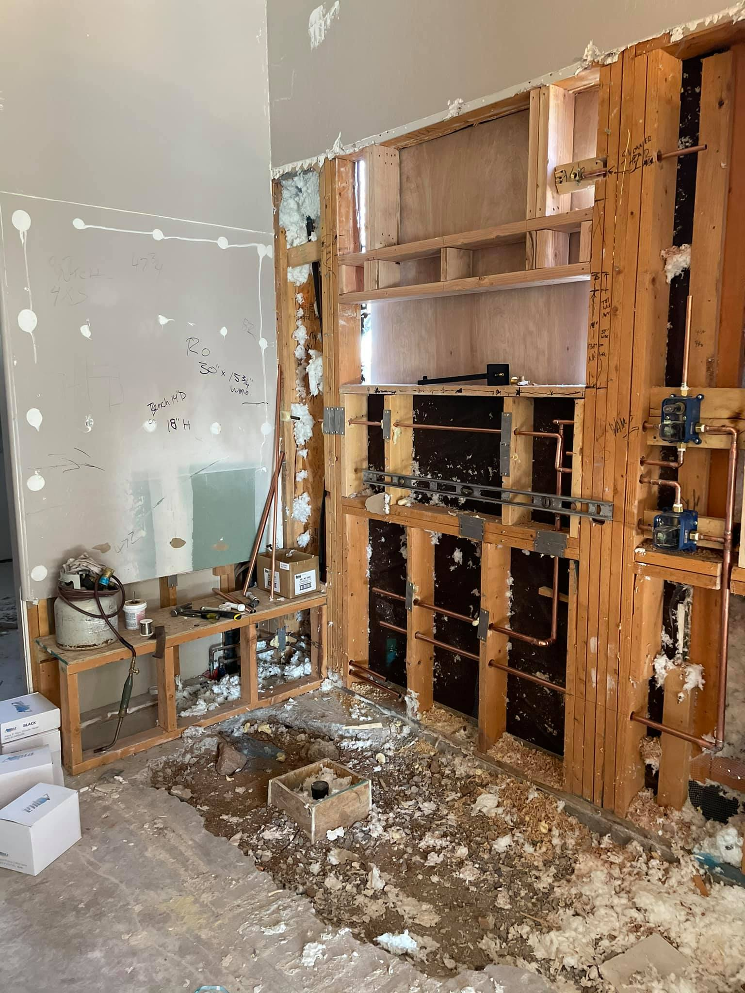 Construction site interior; exposed wood framing for cabinets and shelving, debris on floor, unfinished walls.