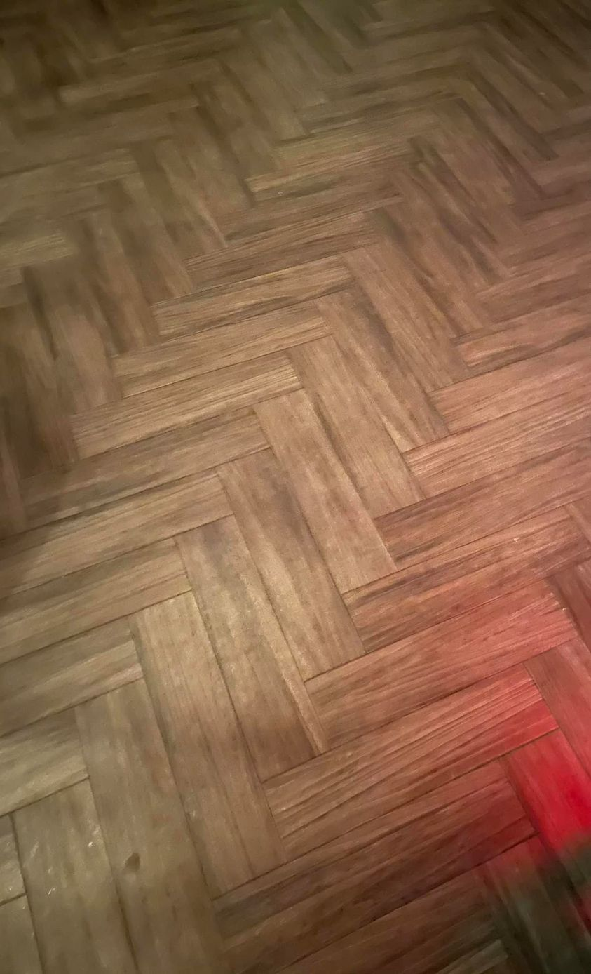 Herringbone pattern wooden floor, brown planks, red light cast.