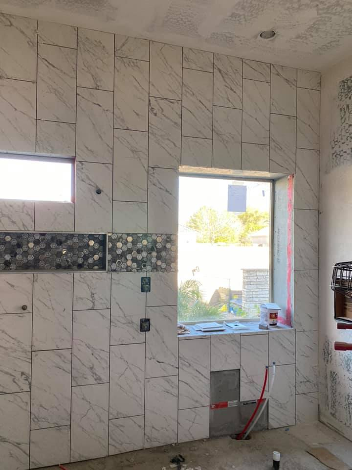 Bathroom with marble tile on the walls, a small window, and a larger window with a view outside.