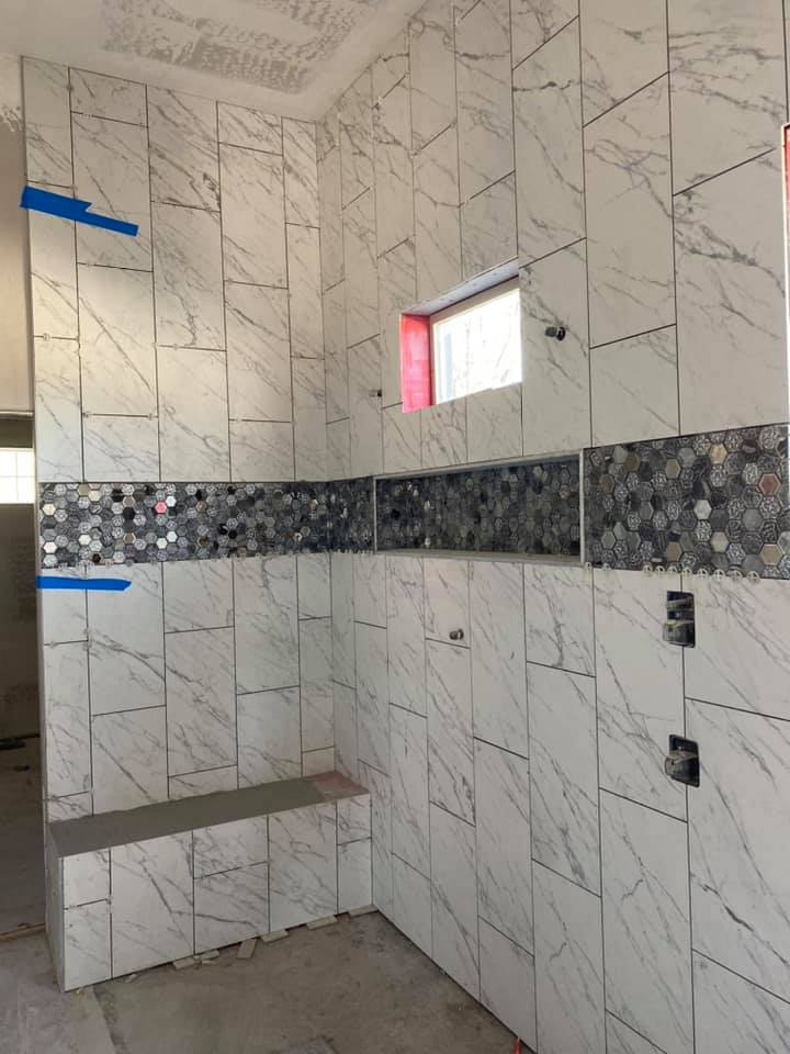 Tiled shower under construction with white marble-like tiles, a mosaic accent, and a built-in bench.