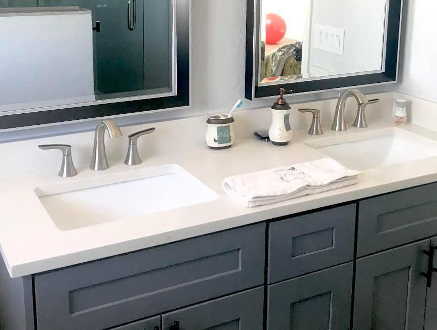 Bathroom vanity with two sinks, gray cabinets, and dark-framed mirrors.