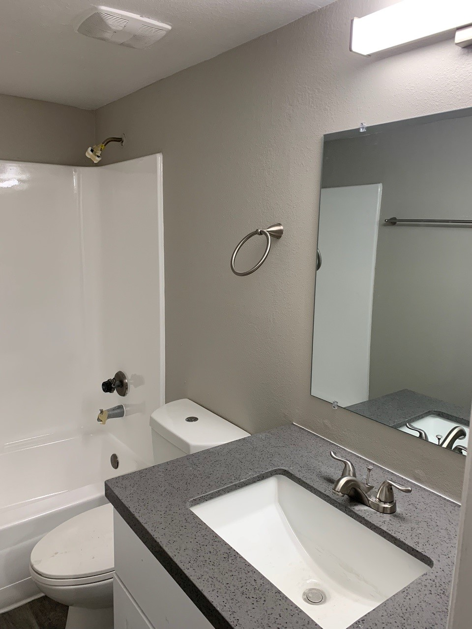 Bathroom with white bathtub, toilet, and vanity with gray countertop and mirror. Gray walls and gold fixtures.