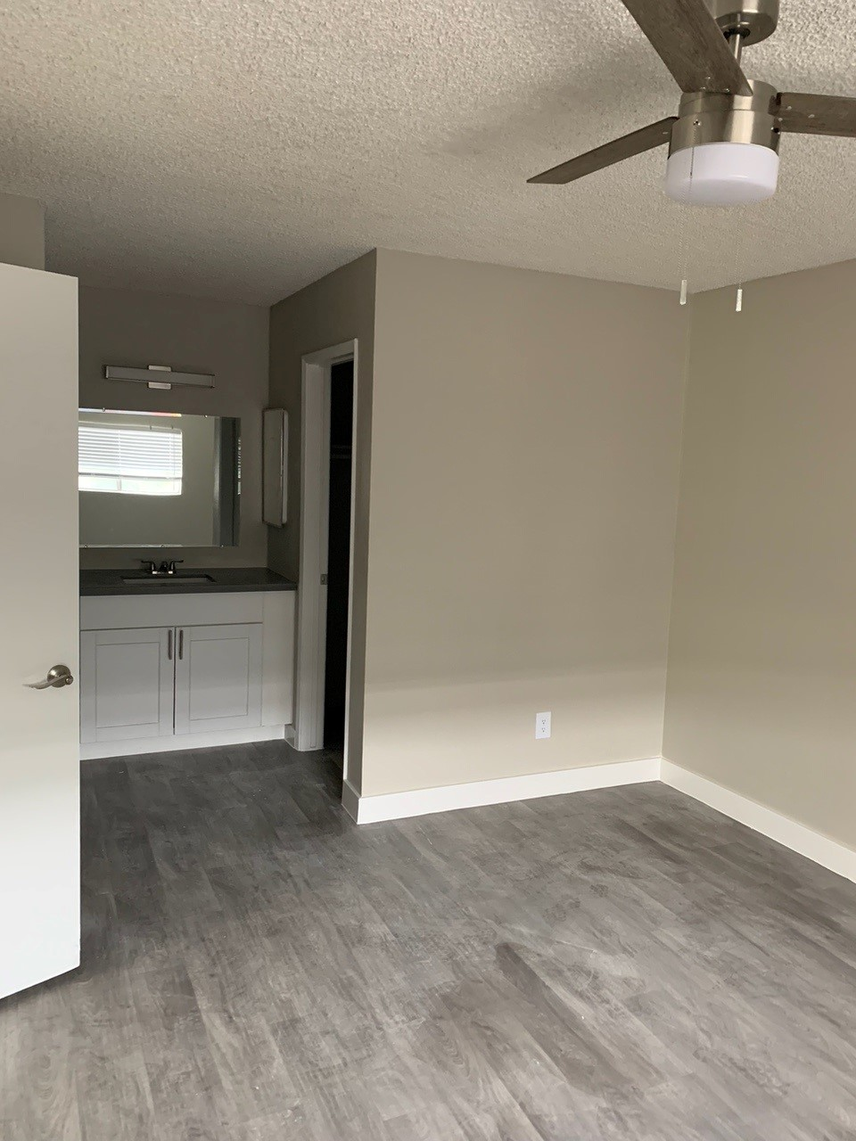 Bedroom with gray flooring, tan walls, and a bathroom visible; ceiling fan.