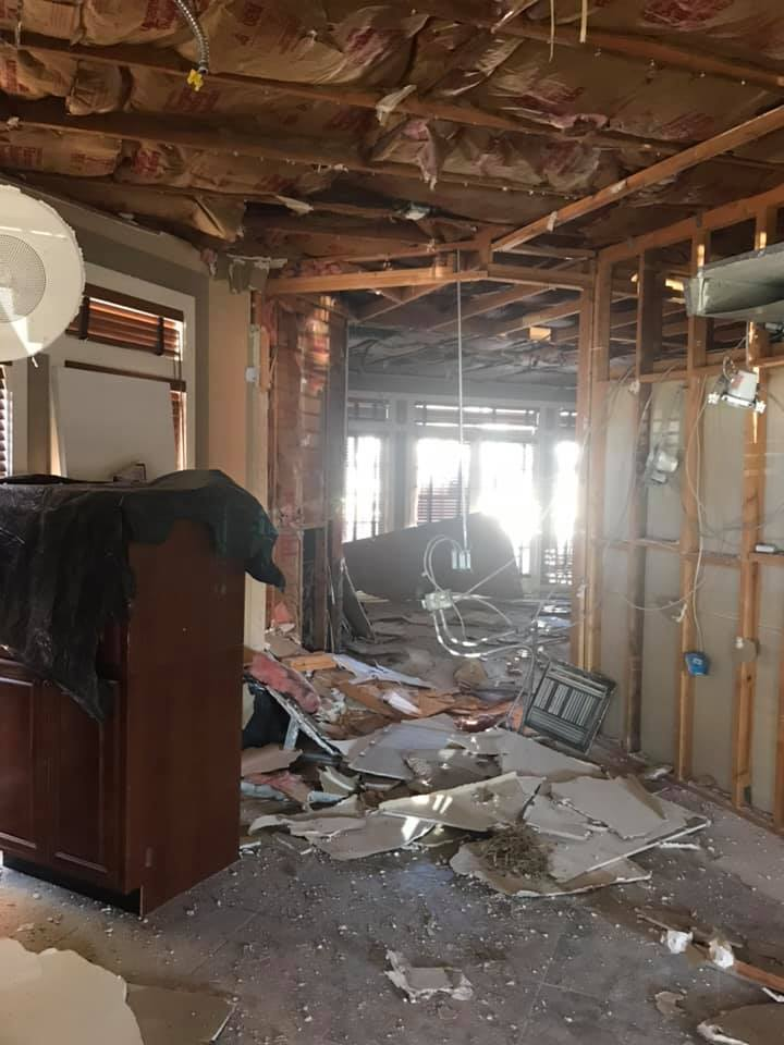 Interior of a house heavily damaged with exposed framing and debris, likely from a disaster.