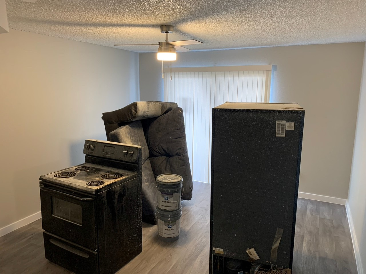 Room with an old stove, a recliner, a fridge, and a paint can, near a sliding glass door.