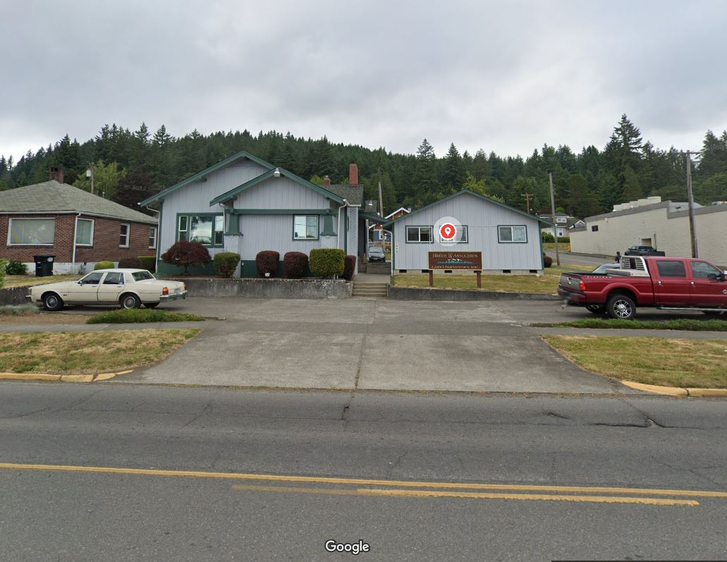 Buildings with a red truck parked to the right. The middle building has a red and white logo. Gray sky.