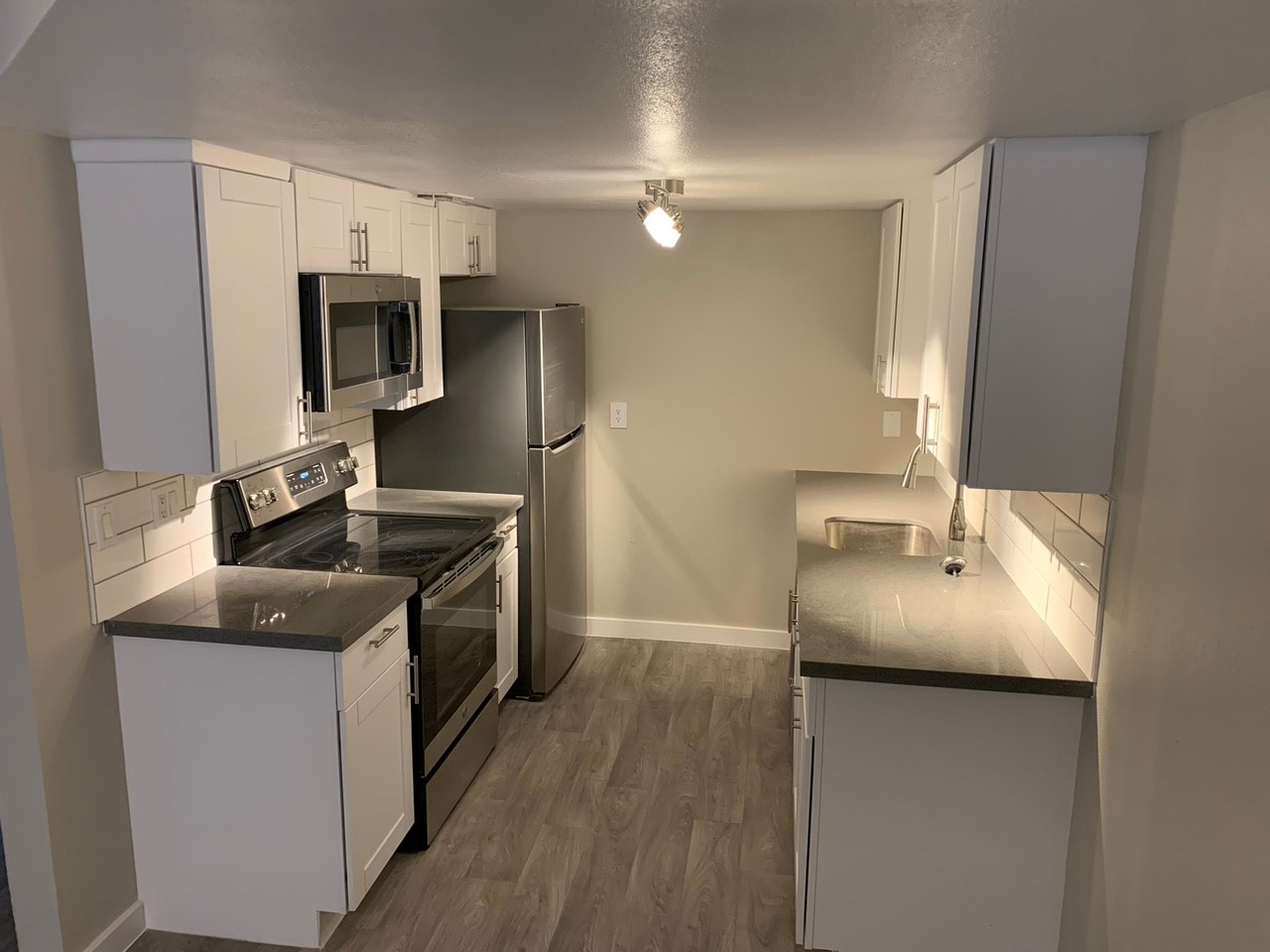 A small, white kitchen with stainless steel appliances and light gray flooring.