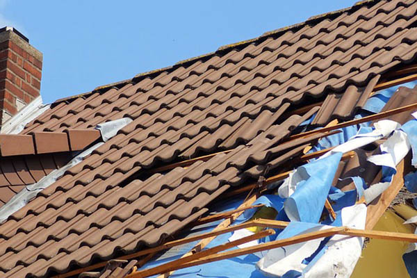 Damaged brown roof with torn blue and white debris, possibly from a storm.