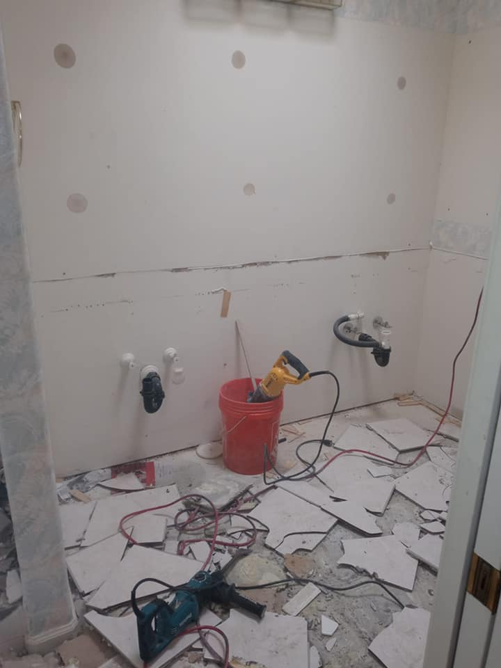 Bathroom under renovation, tiles and tools strewn across the floor, exposed plumbing.