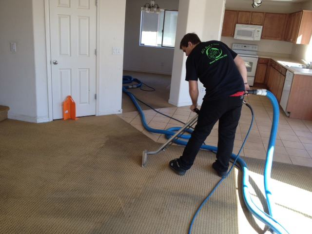 Man steam cleaning carpet in a house, using a hose connected to a machine.