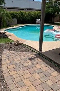 Brick patio leading to a pool with floating tubes, lush greenery in the background.