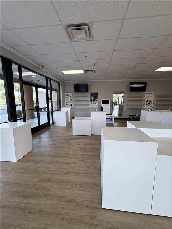 Empty retail space with white display cubes and shelving, wooden floors, and large windows.