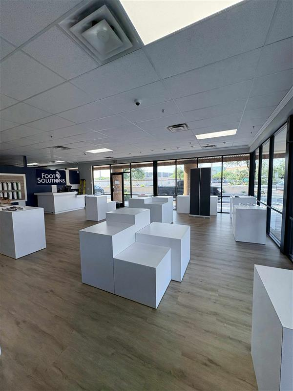 Interior of a store with white display cubes, wood-look flooring, large windows.
