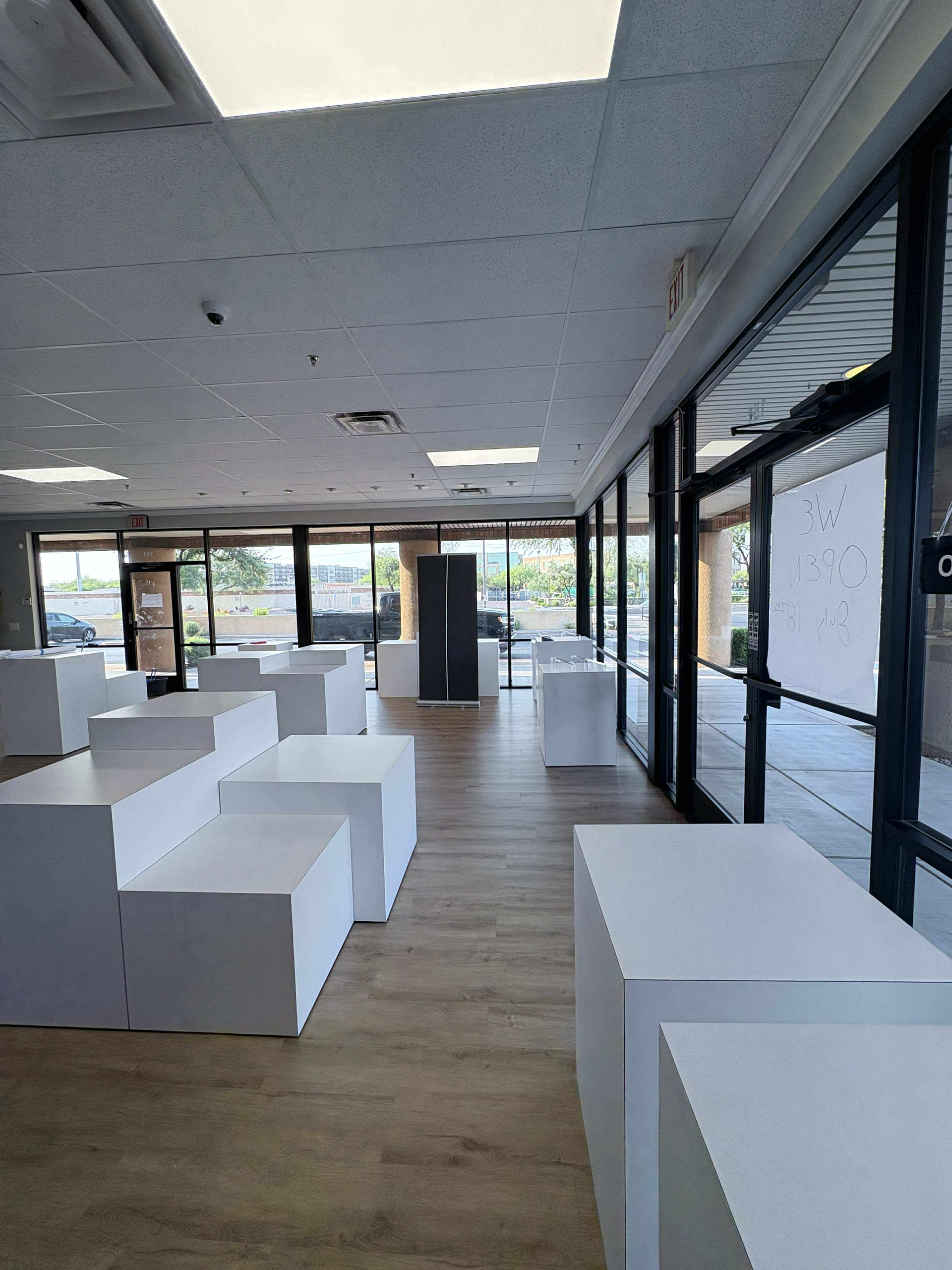 Empty retail space with white display platforms and large windows.