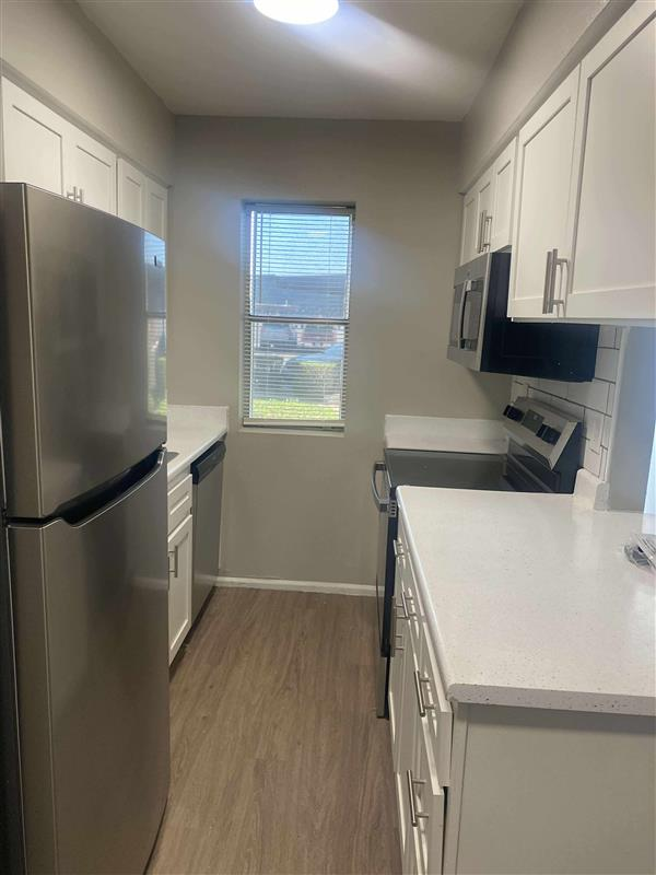 Narrow kitchen with white cabinets, stainless steel appliances, and a window.