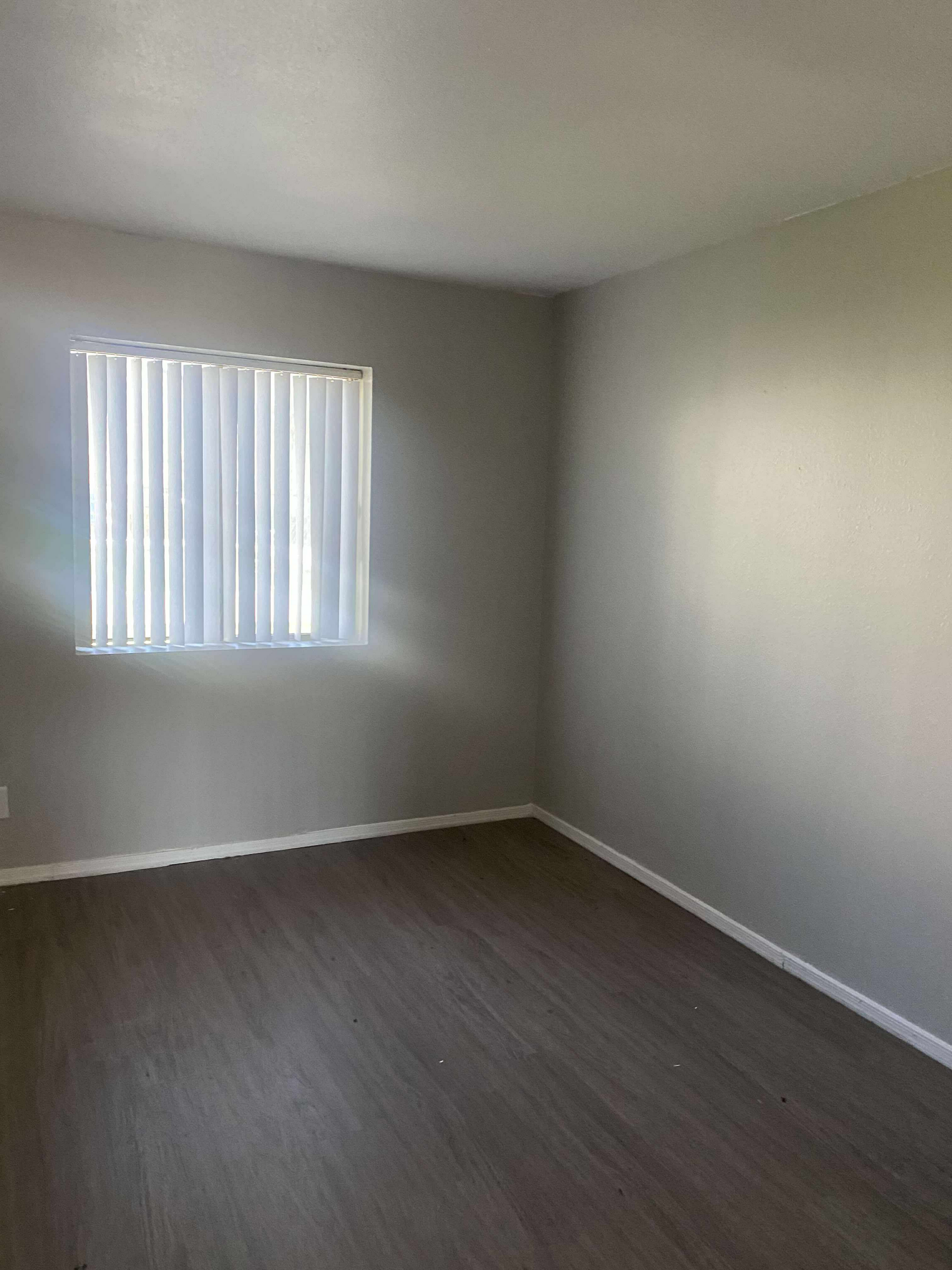 Empty room with gray walls, wood-look floor, and window with blinds.