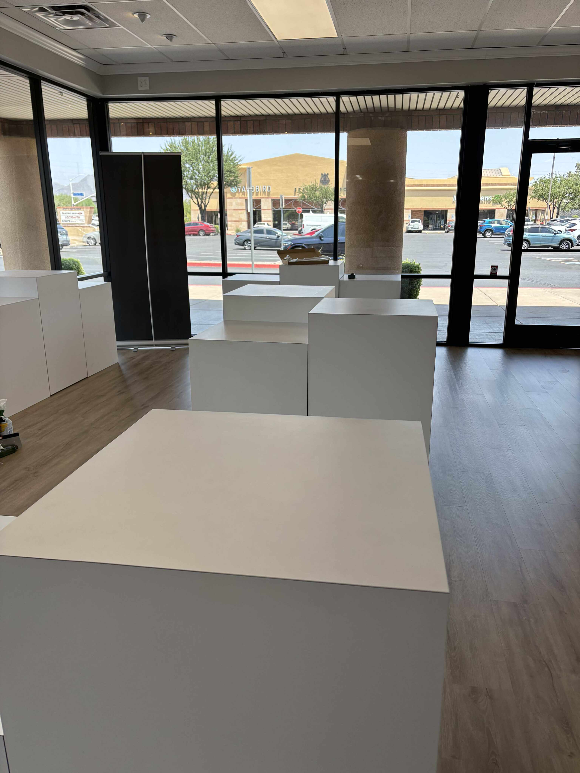 Empty retail space with white display cubes near a large window overlooking a street.