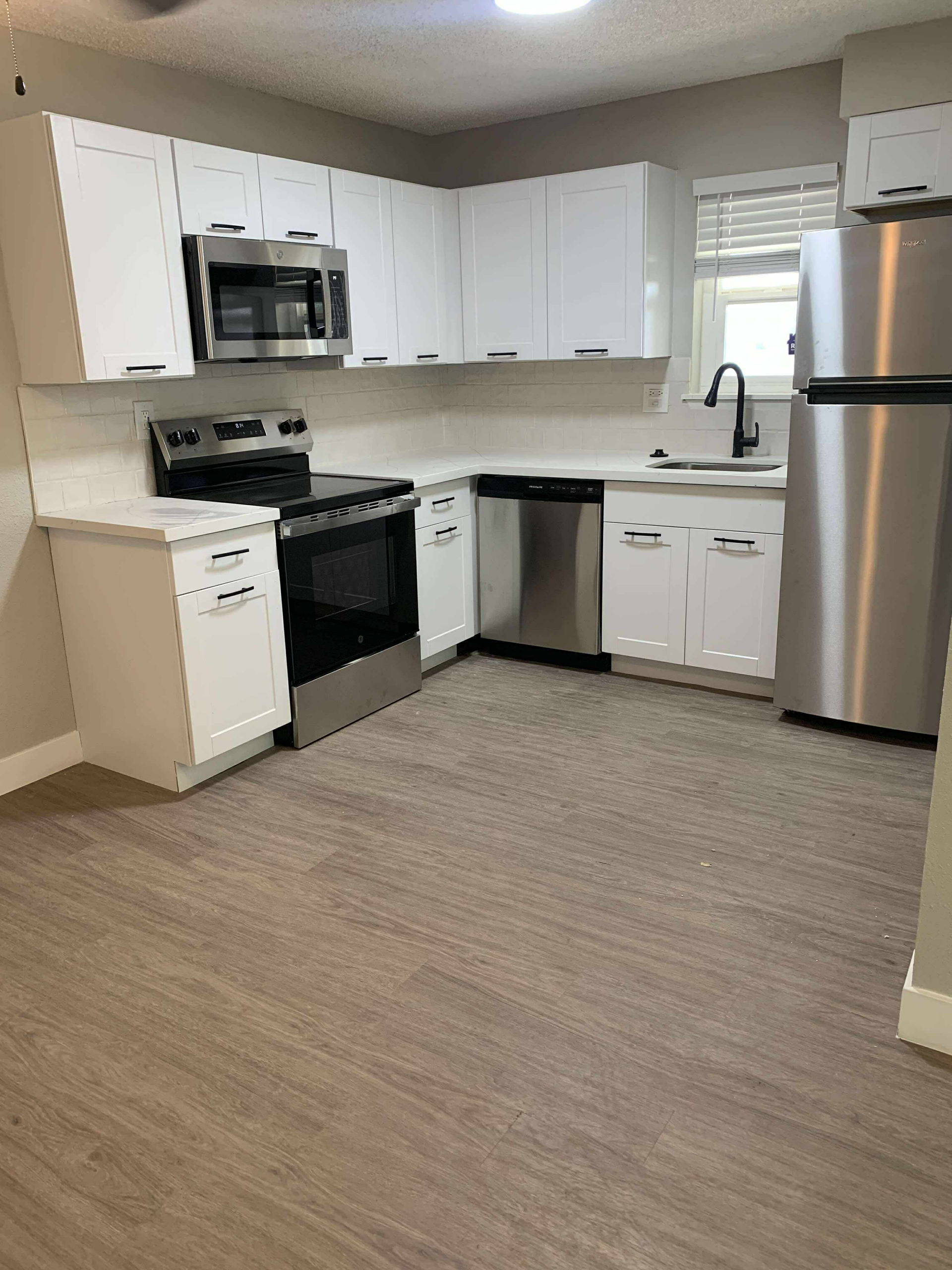 Modern white kitchen with stainless steel appliances and white cabinets.
