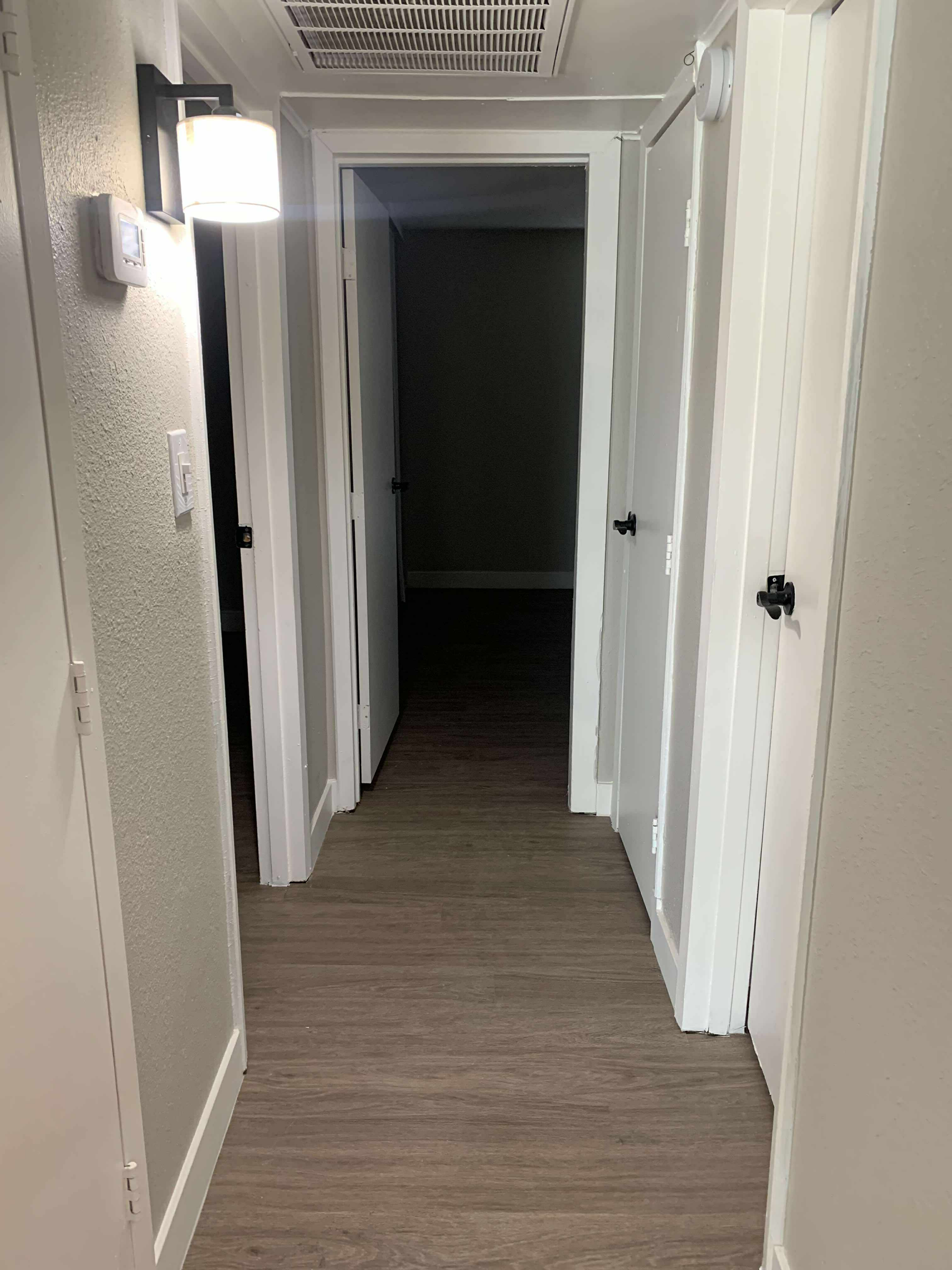 Hallway with wood-look flooring, doors, and a light fixture on the wall.