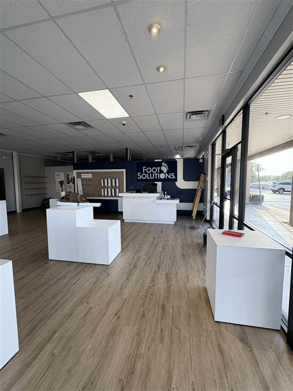 Empty retail space with white display cubes, wood floor, and storefront windows. 